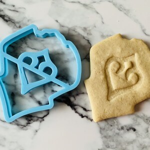May include: A blue plastic cookie cutter shaped like a heart with the number 25 inside. A cookie is shown next to the cutter with the same design imprinted on it.