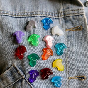 May include: A denim jacket with a variety of colorful, crescent-shaped pins with white zodiac symbols. The pins are arranged in a circle on the jacket.