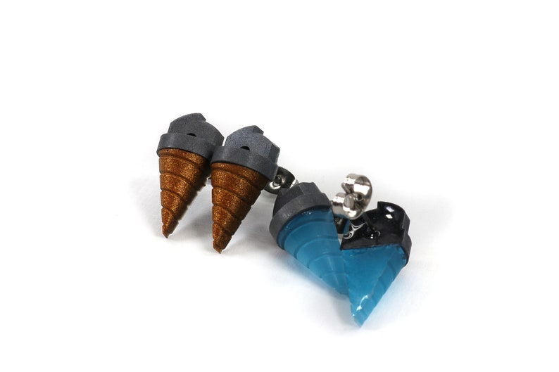 May include: A pair of ice cream cone earrings and a pendant. The earrings feature brown cones with gray tops. The pendant has a blue cone with a black top and silver hardware. The jewelry is set against a white background.