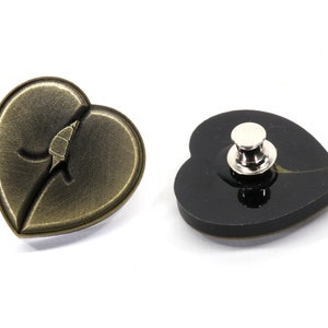 May include: A gold heart-shaped pin with a leaf design and a black heart-shaped pin with a silver pin back.