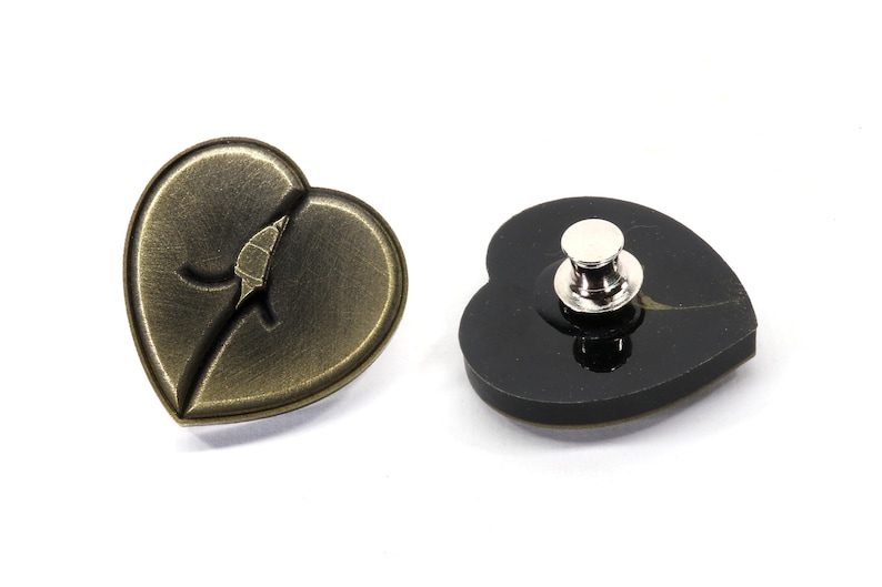 May include: A gold heart-shaped pin with a leaf design and a black heart-shaped pin with a silver pin back.