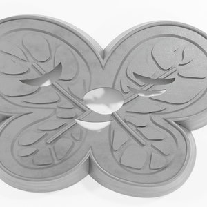 May include: A gray, ceramic butterfly-shaped cookie cutter with a detailed design. The cutter has a symmetrical design with two wings on each side.