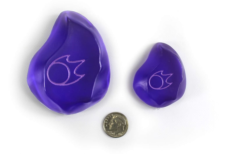 Op de afbeelding: Twee paarse glazen stenen met een roze vlamontwerp. De grotere steen is ongeveer zo groot als een munt van 20 cent.