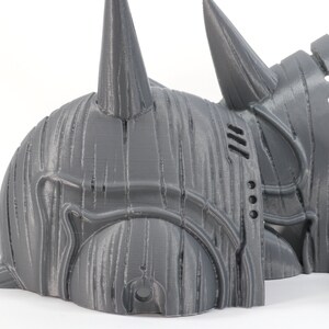 May include: A 3D printed gray helmet with a pointed horn on top. The helmet is made in multiple pieces and has a textured surface.