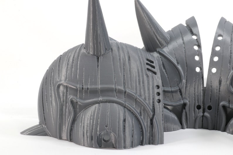 May include: A 3D printed gray helmet with a pointed horn on top. The helmet is made in multiple pieces and has a textured surface.