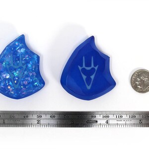 May include: Two blue resin pendants with a white design. One pendant has a sparkly, iridescent finish. The other pendant has a solid blue finish.