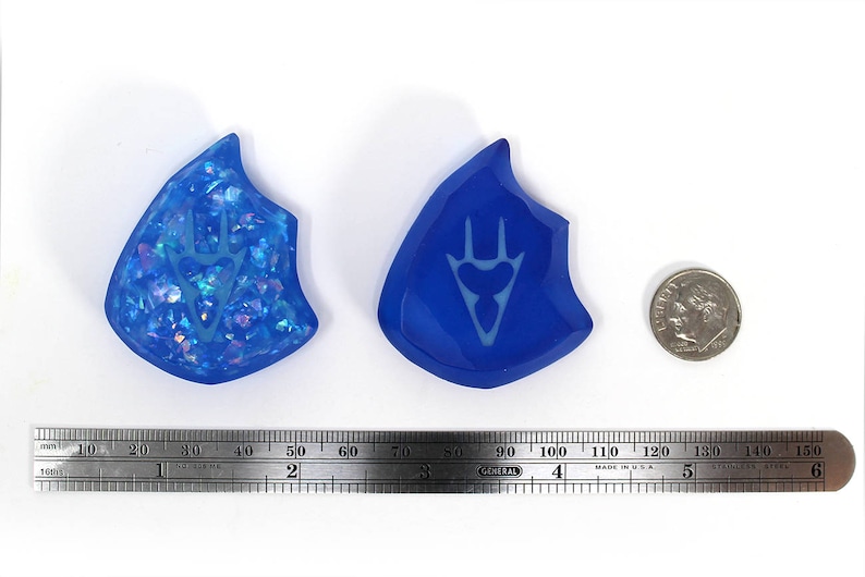 May include: Two blue resin pendants with a white design. One pendant has a sparkly, iridescent finish. The other pendant has a solid blue finish.
