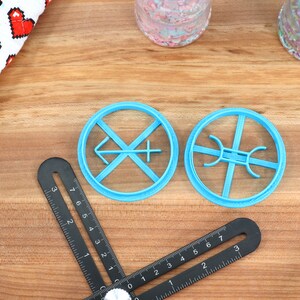May include: Two blue plastic cookie cutters on a wooden surface. One cutter is shaped like a cross with an arrow pointing to the left. The other cutter is shaped like a circle with four spokes.