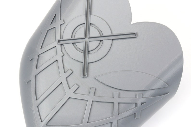 May include: A gray, heart-shaped object with a geometric design. The design includes a crosshair, a circle, and a grid-like pattern. The object has a smooth, slightly curved surface.