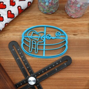 May include: Blue plastic cookie cutter shaped like a stack of pancakes with a smiling face and a drizzle of syrup.