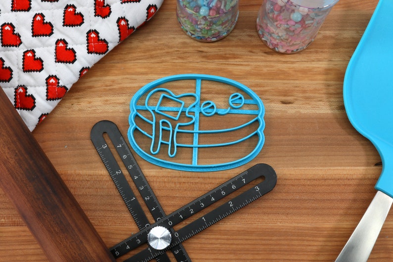 May include: Blue plastic cookie cutter shaped like a stack of pancakes with a smiling face and a drizzle of syrup.