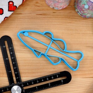 May include: A blue plastic fish-shaped cookie cutter on a wooden surface. The cutter is about 5 inches long and has a small blue circle on the top.