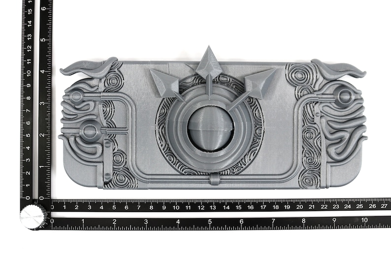 May include: A 3D printed, silver-colored, detailed, intricate, decorative object with a circular design in the center and a series of raised lines and shapes around the edges.
