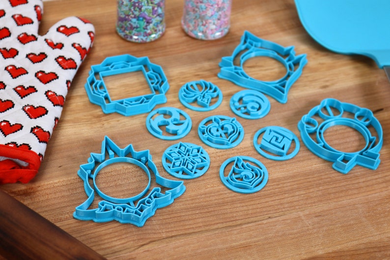 May include: A set of 11 blue plastic cookie cutters with various geometric and floral designs. The cutters are arranged on a wooden surface.