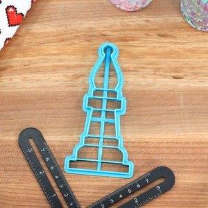 May include: A blue plastic cookie cutter shaped like a chess piece. The piece is a rook or castle.