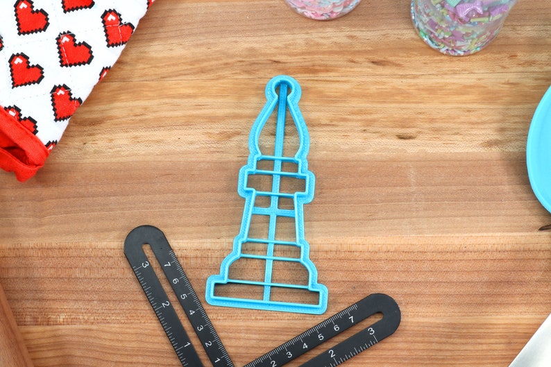 May include: A blue plastic cookie cutter shaped like a chess piece. The piece is a rook or castle.