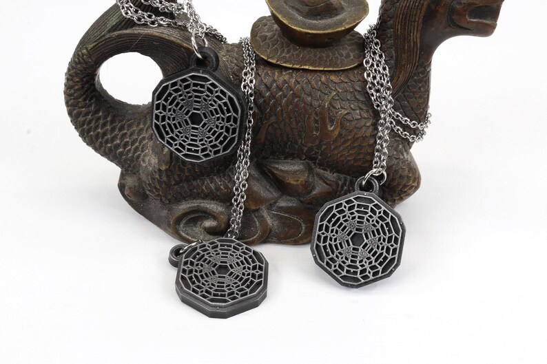 May include: Three silver necklaces with geometric pendant charms. The charms are octagonal and feature a detailed, intricate design.