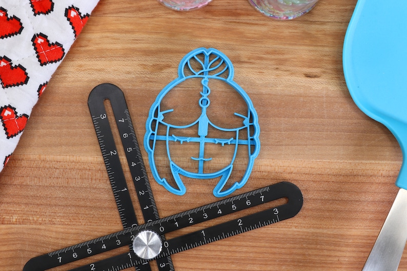 Puede incluir: Un cortador de galletas de pl&aacute;stico azul con forma de mujer de dibujos animados con un mo&ntilde;o en el pelo. El cortador tiene un dise&ntilde;o detallado con rasgos faciales y un atuendo sencillo.