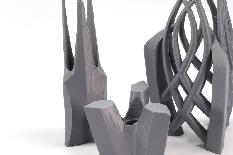 May include: Three gray 3D printed objects. The first object is tall and slender with a pointed top. The second object is a short, wide, and open-topped vase. The third object is a tall, intricate, and open-work sculpture.