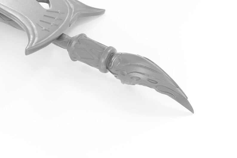 May include: A silver-colored metal spearhead with a detailed, ornate design. The spearhead is pointed and has a sharp tip.