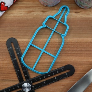 May include: A blue plastic baby bottle cookie cutter on a wooden surface. The cutter has a detailed design with a nipple and a handle.