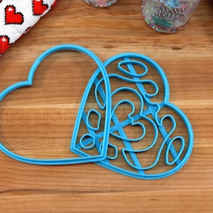 May include: Two blue plastic heart-shaped cookie cutters. One cutter is a simple heart shape, while the other has a more intricate design with multiple smaller hearts inside.