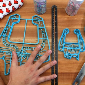 Peut inclure: Deux emportes-pi&egrave;ces en plastique bleu en forme de personnage de jeu vid&eacute;o. Le plus grand emporte-pi&egrave;ce est &agrave; peu pr&egrave;s de la taille de la main d'une personne. Le plus petit emporte-pi&egrave;ce est environ deux fois plus petit que le plus grand. Les deux emportes-pi&egrave;ces sont sur une surface en bois.