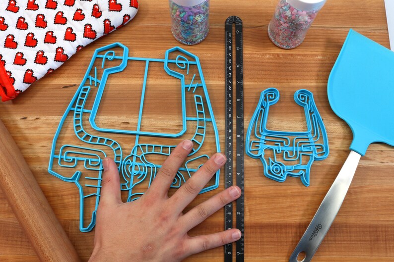 Peut inclure: Deux emportes-pi&egrave;ces en plastique bleu en forme de personnage de jeu vid&eacute;o. Le plus grand emporte-pi&egrave;ce est &agrave; peu pr&egrave;s de la taille de la main d'une personne. Le plus petit emporte-pi&egrave;ce est environ deux fois plus petit que le plus grand. Les deux emportes-pi&egrave;ces sont sur une surface en bois.