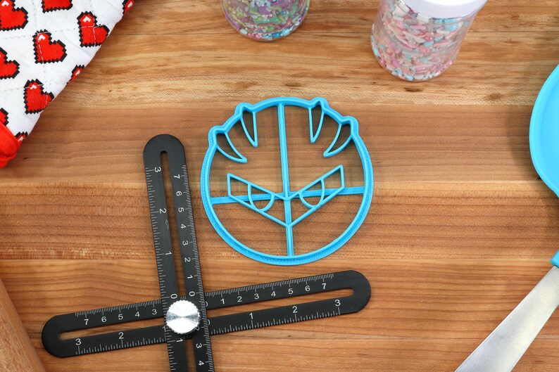 May include: Blue plastic cookie cutter shaped like a cartoon face with angry eyes and a wide mouth.