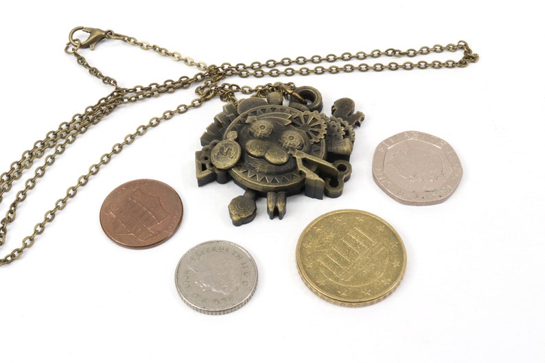 May include: A bronze necklace with a detailed steampunk-style pendant featuring a cartoon lion face surrounded by gears and other mechanical elements. The pendant is hanging with a chain and is surrounded by four coins.
