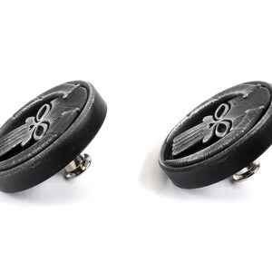 May include: Two black metal buttons with a silver skull design. Each button has a pin on the back.