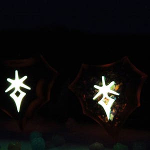 May include: Two dark brown, resin-like, circular objects with a white, glowing, star-shaped symbol in the centre. The symbol is a stylized star with a diamond in the centre.