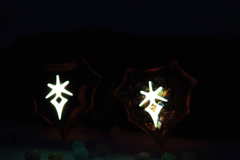 May include: Two dark brown, resin-like, circular objects with a white, glowing, star-shaped symbol in the centre. The symbol is a stylized star with a diamond in the centre.