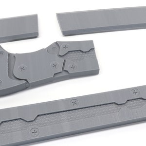 May include: Five gray plastic pieces of a disassembled knife. The pieces have a textured surface and are held together by screws.