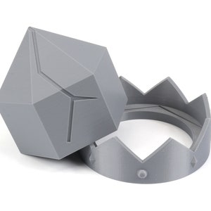May include: A gray, geometric, diamond-shaped object and a gray crown-shaped ring. Both objects are made of plastic.