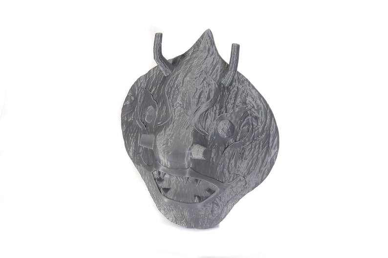 Puede incluir: Una m&aacute;scara gris impresa en 3D con una expresi&oacute;n feroz. La m&aacute;scara tiene una superficie texturizada y presenta dientes afilados, cuernos y ojos.