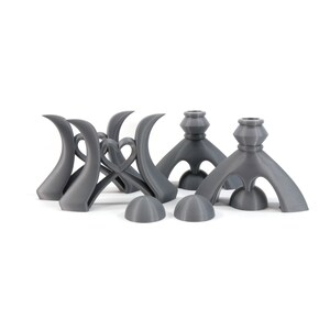 May include: Set of five gray 3D printed candle holders. Two of the holders have a unique, abstract design with three legs. The other three holders have a more traditional design with a round base and a single stem.