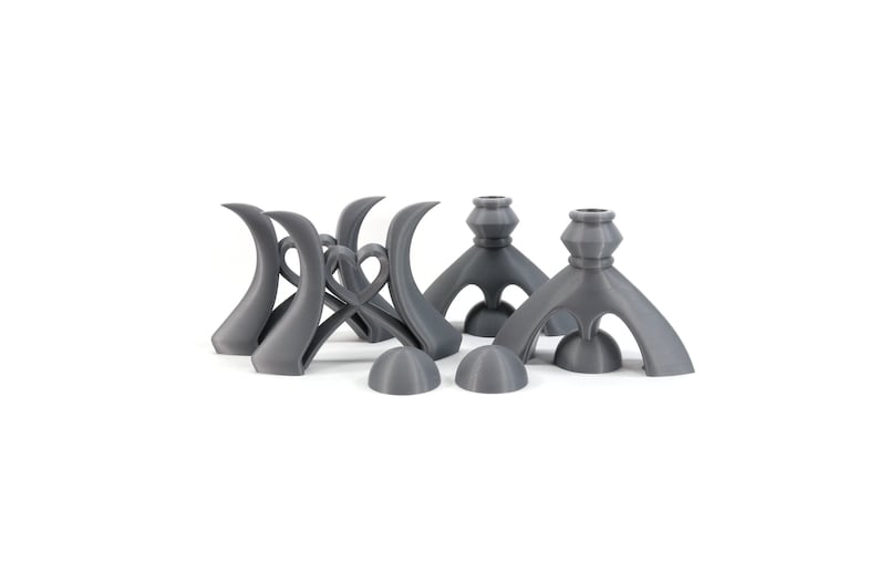 May include: Set of five gray 3D printed candle holders. Two of the holders have a unique, abstract design with three legs. The other three holders have a more traditional design with a round base and a single stem.
