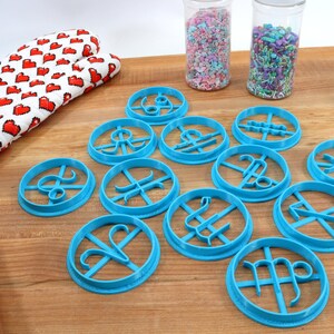 May include: A set of 12 blue plastic cookie cutters shaped like the astrological signs. The cutters are arranged on a wooden surface.