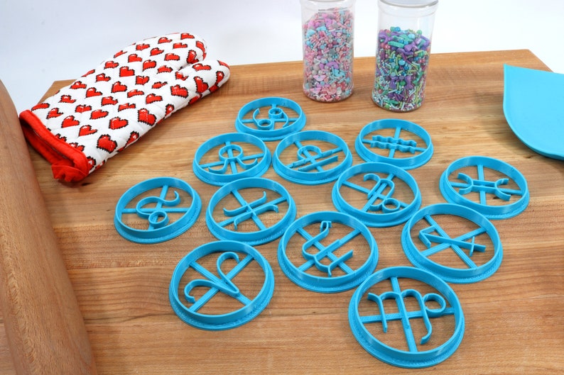 May include: A set of 12 blue plastic cookie cutters shaped like the astrological signs. The cutters are arranged on a wooden surface.