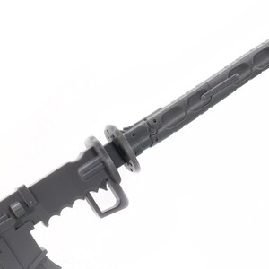 Puede incluir: Un modelo de pl&aacute;stico gris de un arma futurista con una hoja y un mango. El arma tiene un dise&ntilde;o detallado con surcos intrincados y una superficie texturizada.