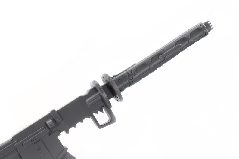 Puede incluir: Un modelo de pl&aacute;stico gris de un arma futurista con una hoja y un mango. El arma tiene un dise&ntilde;o detallado con surcos intrincados y una superficie texturizada.