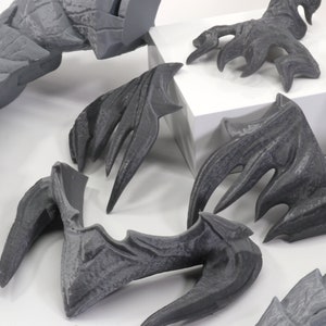 May include: A set of gray 3D printed dragon wings, claws, and tail pieces. The pieces are detailed with scales and spikes.