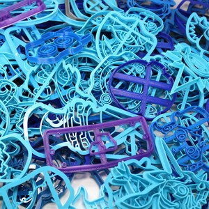 Op de afbeelding: Een grote verzameling blauwe en paarse plastic koekjesvormen in verschillende vormen en maten. De vormen zijn in een willekeurige stapel gerangschikt.
