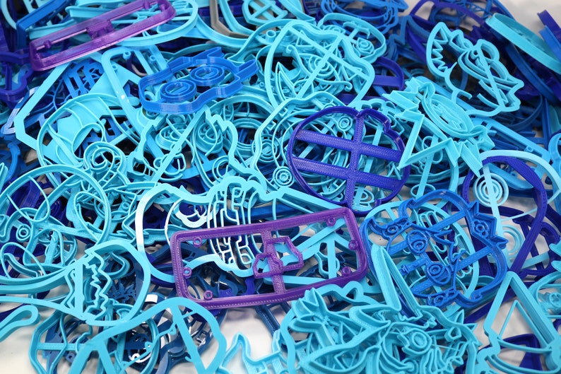 Op de afbeelding: Een grote verzameling blauwe en paarse plastic koekjesvormen in verschillende vormen en maten. De vormen zijn in een willekeurige stapel gerangschikt.