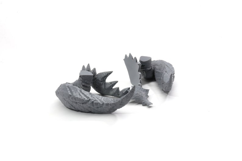 May include: Gray plastic model of a dinosaur tail with spikes and textured skin. The tail is broken into several pieces.