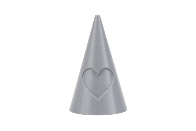 May include: A gray ceramic ring holder shaped like a cone with a heart cutout on the front.