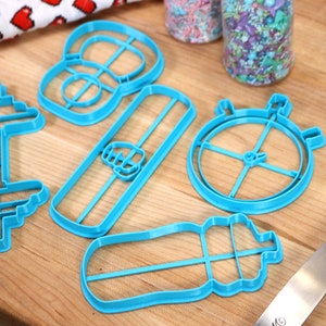 May include: A set of five blue plastic cookie cutters shaped like a dumbbell, a water bottle, a protein bar, a stopwatch, and a weight plate.