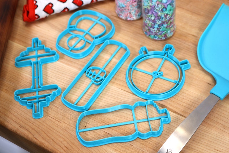May include: A set of five blue plastic cookie cutters shaped like a dumbbell, a water bottle, a protein bar, a stopwatch, and a weight plate.