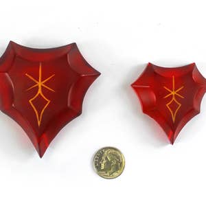 May include: Two red, crystal-like shields with a gold symbol in the center. The shields are different sizes.